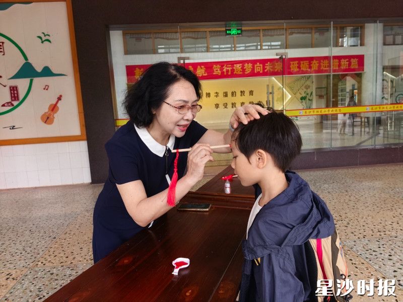 图为长沙市湘龙小学老师手执朱砂，为学童点上朱砂痣，寄托开启智慧、明理向善的美好期许。