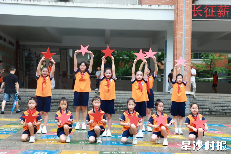 长沙市龙塘小学的同学们手持红色星形道具在校园前合影，定格 “星少年” 向阳成长的瞬间。